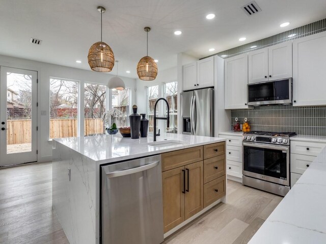 kitchen featuring light stone countertops, appliances with stainless steel finishes, sink, white cabinets, and hanging light fixtures