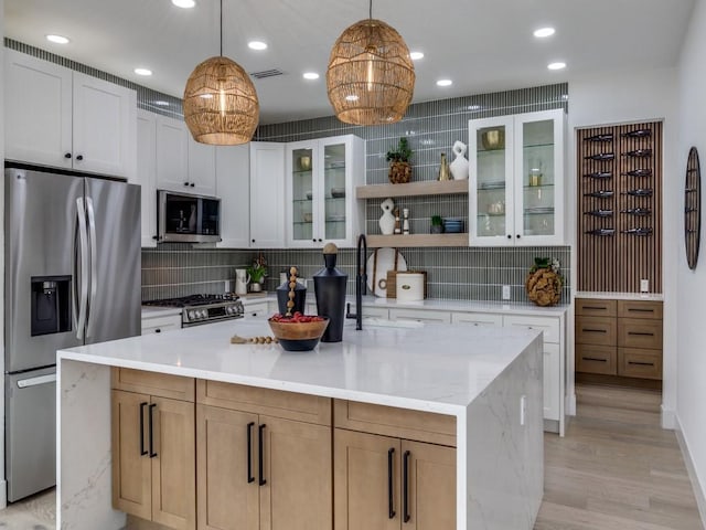 kitchen featuring appliances with stainless steel finishes, tasteful backsplash, white cabinetry, and a kitchen island with sink