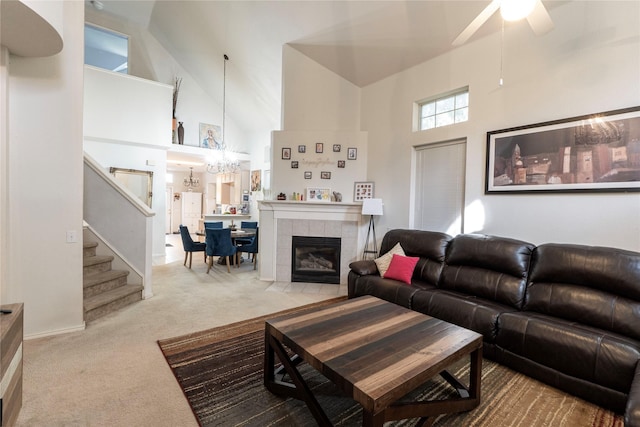 carpeted living room featuring ceiling fan with notable chandelier, high vaulted ceiling, and a tile fireplace