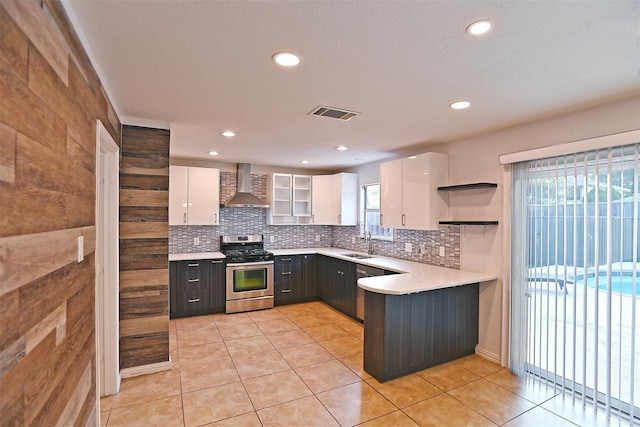 kitchen featuring a sink, wall chimney range hood, white cabinets, light countertops, and gas range