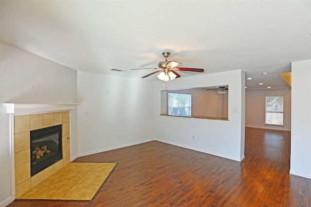 unfurnished living room featuring a tiled fireplace, ceiling fan, dark hardwood / wood-style flooring, and a healthy amount of sunlight