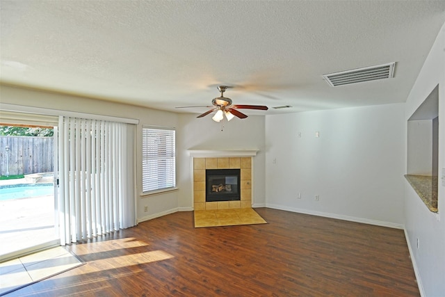 unfurnished living room featuring a tiled fireplace, ceiling fan, a textured ceiling, and dark hardwood / wood-style flooring