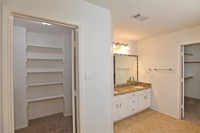 full bathroom with a spacious closet, visible vents, baseboards, double vanity, and a sink