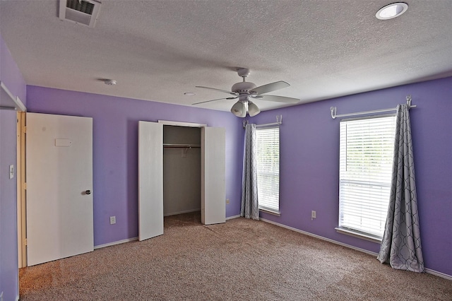 unfurnished bedroom featuring visible vents, carpet floors, a closet, a textured ceiling, and a ceiling fan