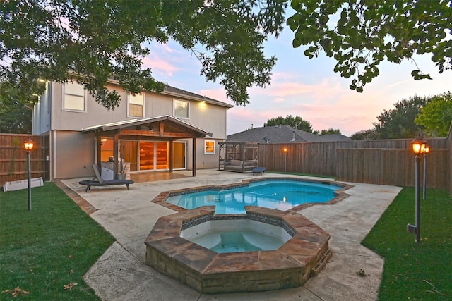 pool at dusk with a patio area, a lawn, and an in ground hot tub