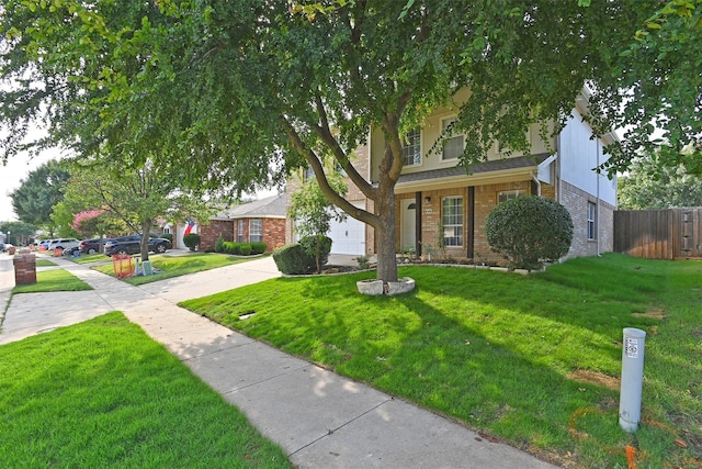 view of property hidden behind natural elements with brick siding, concrete driveway, a front yard, and fence