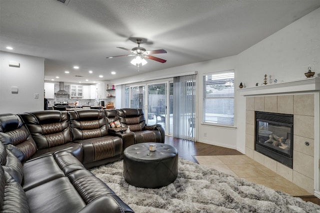 living room featuring a tiled fireplace, light tile patterned floors, and ceiling fan