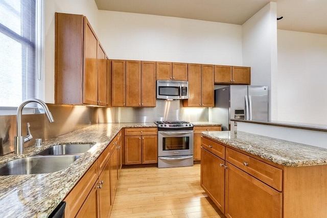 kitchen with sink, stainless steel appliances, light stone counters, a towering ceiling, and light wood-type flooring