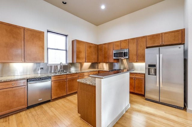 kitchen with sink, stainless steel appliances, a high ceiling, light hardwood / wood-style floors, and a kitchen island