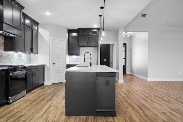 kitchen with decorative backsplash, stainless steel range, a kitchen island with sink, sink, and hanging light fixtures