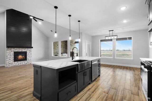 kitchen featuring a stone fireplace, ceiling fan, an island with sink, decorative light fixtures, and stainless steel appliances