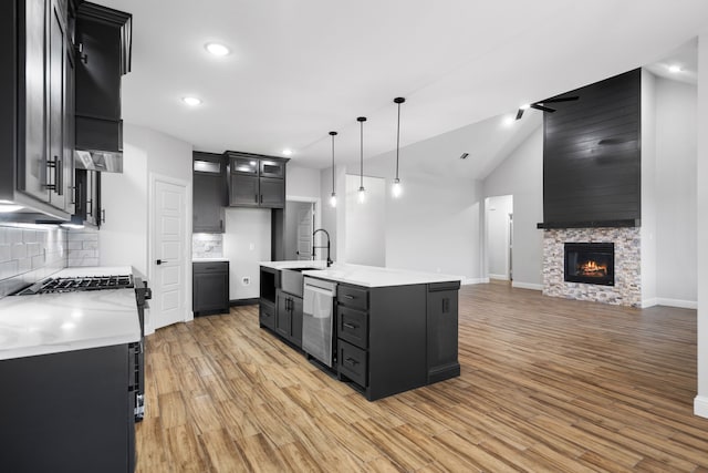 kitchen featuring lofted ceiling, backsplash, a kitchen island with sink, a stone fireplace, and decorative light fixtures