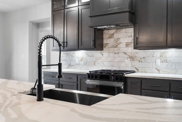 kitchen featuring light stone countertops, backsplash, stainless steel gas range oven, dark brown cabinetry, and ventilation hood