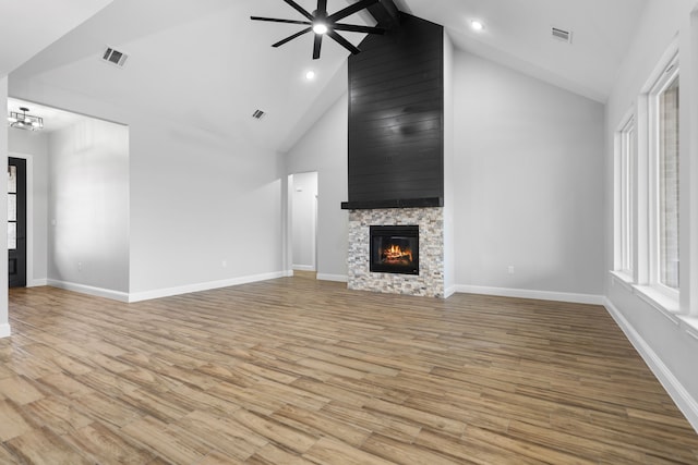 unfurnished living room with ceiling fan with notable chandelier, high vaulted ceiling, beamed ceiling, a fireplace, and light hardwood / wood-style floors