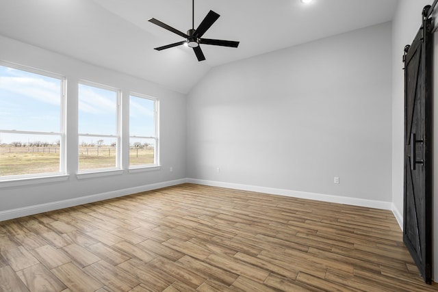 spare room featuring a barn door, vaulted ceiling, and ceiling fan