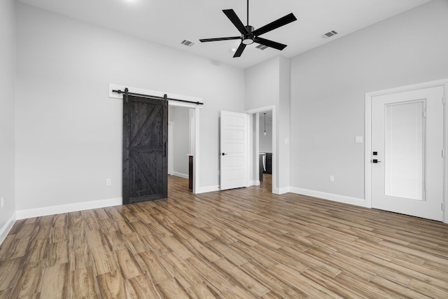 unfurnished bedroom featuring a barn door, ceiling fan, and light wood-type flooring