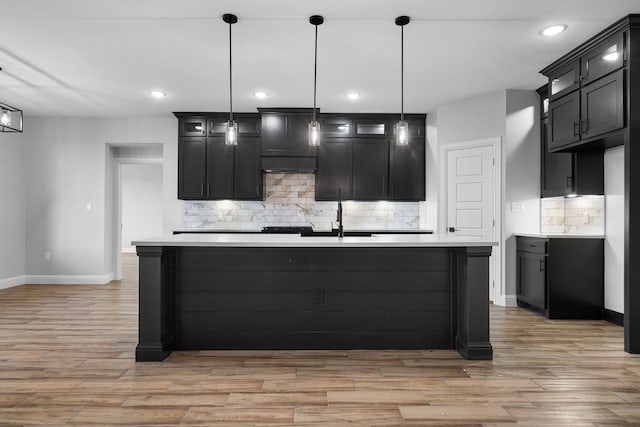 kitchen featuring backsplash, a kitchen island with sink, and pendant lighting