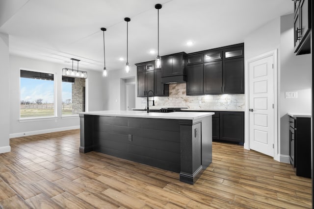 kitchen with decorative light fixtures, backsplash, a center island with sink, and sink