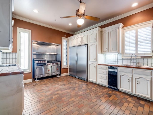 kitchen featuring backsplash, ornamental molding, appliances with stainless steel finishes, tile counters, and white cabinets