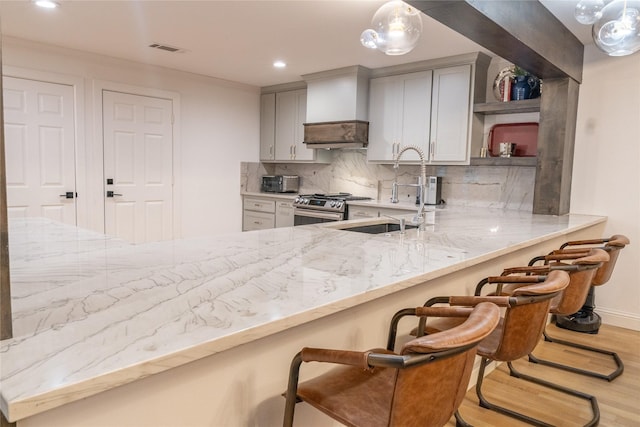 kitchen with premium range hood, sink, stainless steel gas range, tasteful backsplash, and a breakfast bar area