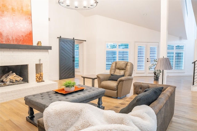 living room featuring a fireplace, a barn door, high vaulted ceiling, and light hardwood / wood-style flooring