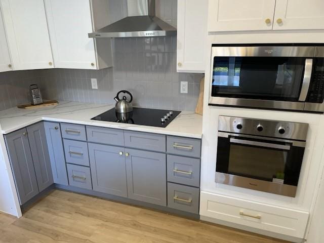 kitchen with decorative backsplash, black electric stovetop, wall chimney exhaust hood, stainless steel oven, and white cabinetry