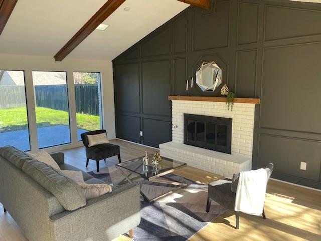 living room with light hardwood / wood-style flooring, lofted ceiling with beams, and a brick fireplace