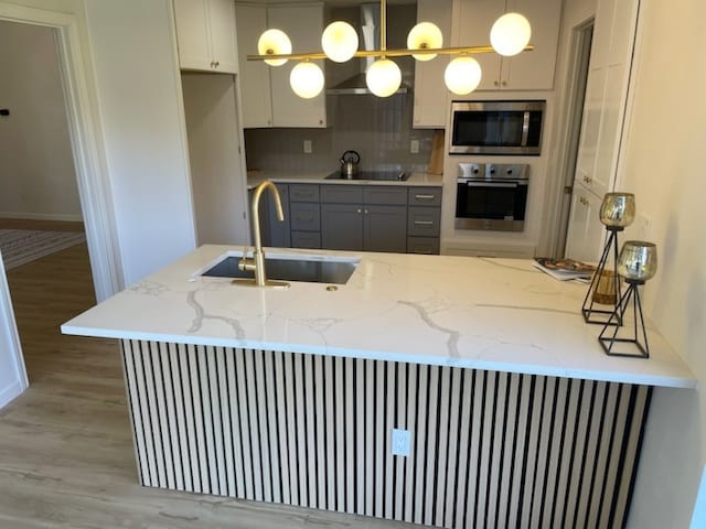 kitchen with light stone countertops, sink, stainless steel appliances, light hardwood / wood-style floors, and pendant lighting