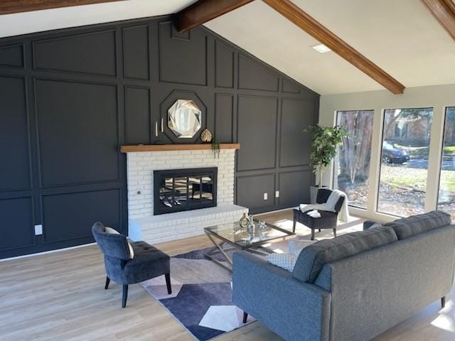 living room featuring vaulted ceiling with beams, light wood-type flooring, and a brick fireplace