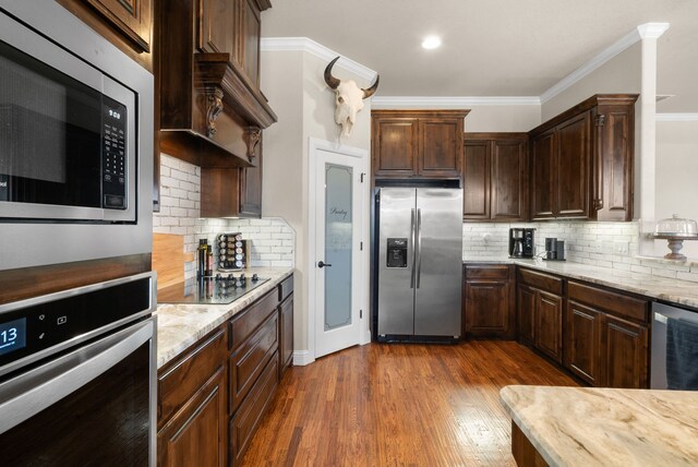 kitchen featuring crown molding, light stone countertops, appliances with stainless steel finishes, tasteful backsplash, and dark hardwood / wood-style flooring