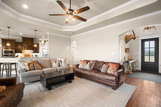 living room featuring a tray ceiling, dark hardwood / wood-style floors, ornamental molding, and ceiling fan