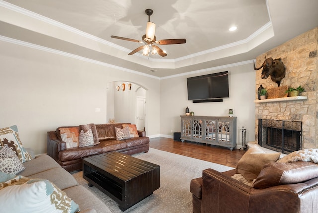 living room with a tray ceiling, a stone fireplace, ornamental molding, and hardwood / wood-style flooring