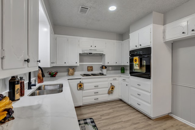 kitchen with white cabinetry, black oven, a textured ceiling, and light hardwood / wood-style flooring