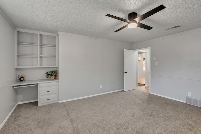 carpeted empty room featuring ceiling fan, built in desk, ornamental molding, and a textured ceiling