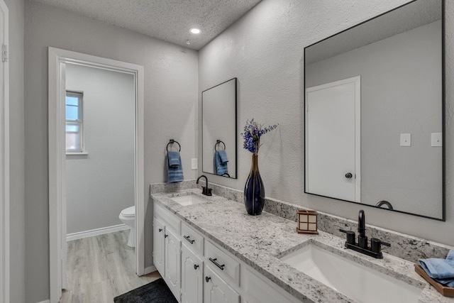 bathroom with hardwood / wood-style flooring, vanity, toilet, and a textured ceiling