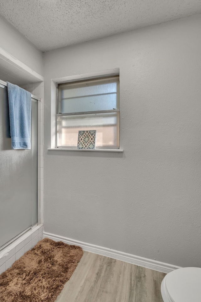 bathroom featuring hardwood / wood-style floors, an enclosed shower, a textured ceiling, and toilet