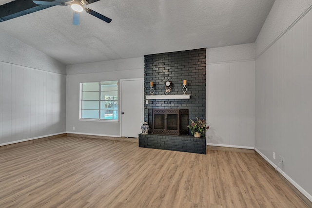 unfurnished living room featuring lofted ceiling, a brick fireplace, a textured ceiling, ceiling fan, and light hardwood / wood-style floors