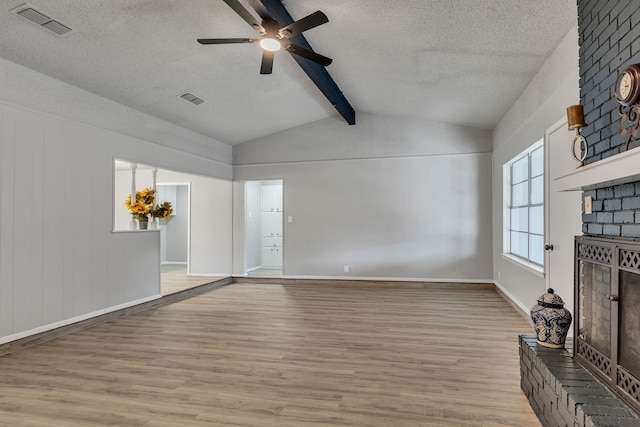 unfurnished living room featuring light hardwood / wood-style flooring, ceiling fan, vaulted ceiling with beams, a fireplace, and a textured ceiling