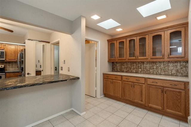 kitchen featuring light tile patterned floors, ceiling fan, appliances with stainless steel finishes, backsplash, and dark stone counters