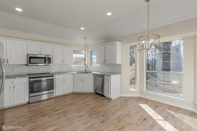 kitchen with appliances with stainless steel finishes, pendant lighting, sink, white cabinets, and light hardwood / wood-style floors