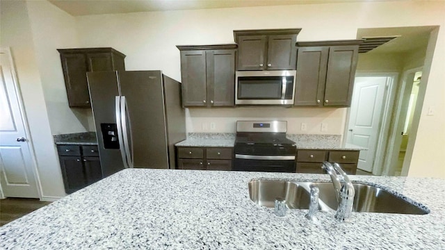 kitchen featuring light stone countertops, appliances with stainless steel finishes, dark brown cabinetry, and sink