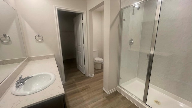 bathroom featuring toilet, wood-type flooring, vanity, and a shower with door