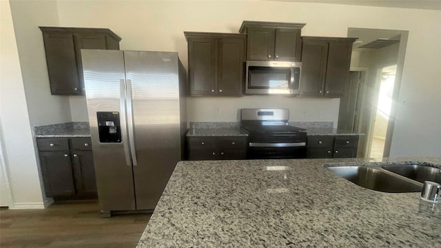 kitchen with light stone counters, stainless steel appliances, dark hardwood / wood-style floors, and dark brown cabinetry