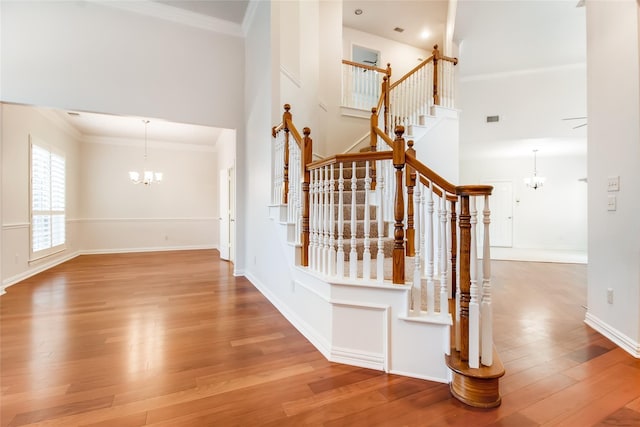 stairs featuring hardwood / wood-style flooring, ornamental molding, and an inviting chandelier