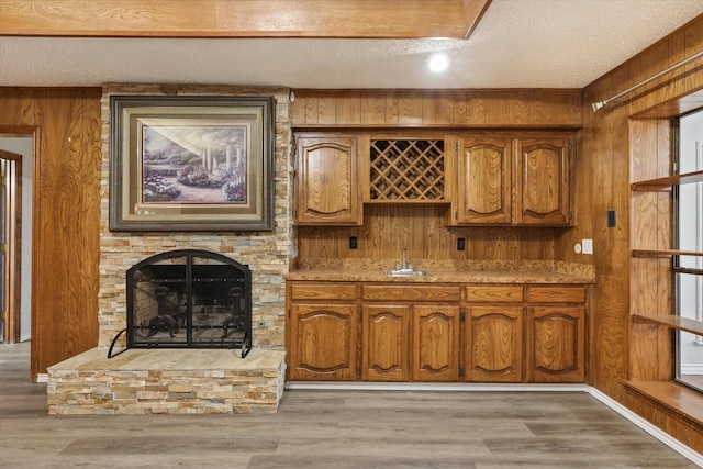 kitchen featuring a textured ceiling, sink, hardwood / wood-style flooring, a stone fireplace, and wood walls