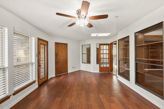 unfurnished room featuring a skylight, ceiling fan, french doors, dark wood-type flooring, and a textured ceiling