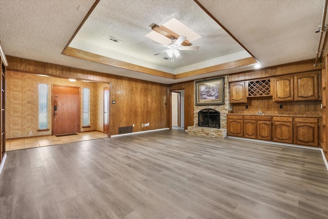 unfurnished living room featuring a fireplace, a raised ceiling, ceiling fan, and wood walls