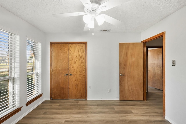 unfurnished bedroom with multiple windows, a closet, ceiling fan, and hardwood / wood-style flooring