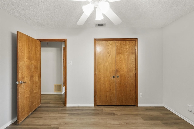 unfurnished bedroom featuring a textured ceiling, dark hardwood / wood-style flooring, a closet, and ceiling fan