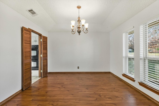 spare room with dark hardwood / wood-style flooring, a textured ceiling, and an inviting chandelier